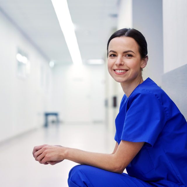 clinic, profession, people, health care and medicine concept - smiling female nurse at hospital corridor