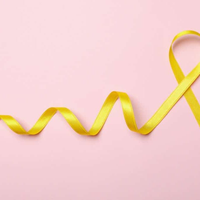 Yellow awareness ribbon on pink background, space for text